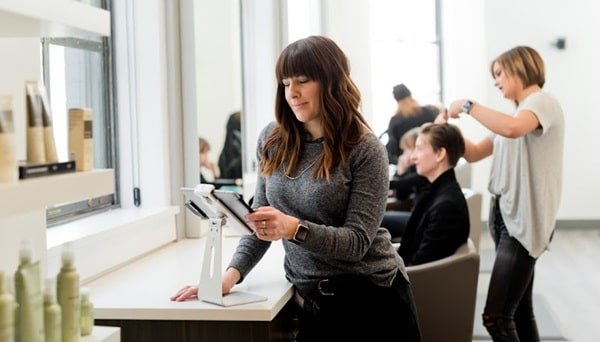 A woman sits in a salon, focused on a tablet, exploring AI integration features for beauty services